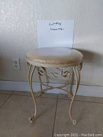 Cream-colored metal vanity stool with cushioned round seat covered by a protective plastic film.