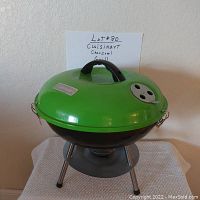 Front side view of Cuisinart portable charcoal picnic grill showing green lid with vent, handle, black base and silver tripod legs with ash catcher