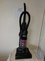 Photo of upright Eureka vacuum cleaner showing the full unit with hose attached and dust container with purple accents.