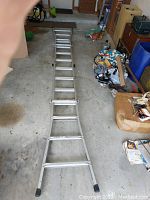 Full length straightened aluminum folding ladder with wide rungs and rubber feet on a garage floor.