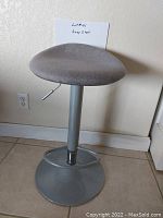 Gray bar stool with padded fabric seat, metal base, height adjustment lever and footrest ring