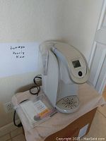 Photo of beige Keurig K-Cup coffee maker on table with power cord and instruction manual.