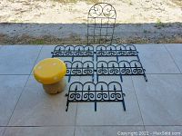 Photo shows yellow mushroom stool, five pieces of black plastic garden edging, and one black metal trellis placed on tiled floor.