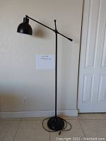 Full view of the tall black reading lamp with adjustable arm and round base next to a white wall and door.