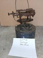 Photo of vintage cast iron gas stove with attached metal fuel tank, pressure gauge, and adjustment knob showing overall condition and details.