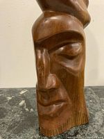 Close-up photo of one carved face showing detailed facial features and polished teak wood grain.