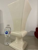 Full side view of the large white Haeger vase with water bottle for scale, showing the angular flared shape and square base with chipping on the base corner.