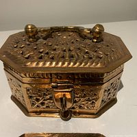 Front view of handmade octagonal copper box showing embossed floral pattern, rounded knobs on lid and locking latch.