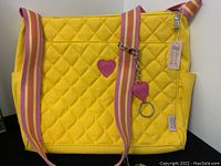 Front view of yellow quilted cross-body bag with pink-striped adjustable strap, side pockets, and attached branded keychain charms.