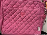 Close-up of the pink quilted front of cross-body bag showing heart-shaped Jeanne Lottie logo and zipper pocket