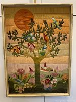 Full view of large needlepoint artwork framed, featuring tree with birds and sun motif.