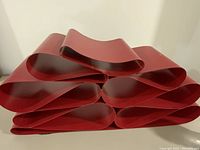 Front view of large red metal abstract sculpture showing stacked flat metal loops and curved design.