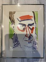 Framed watercolour painting showcasing a male face with bold color blocking and expressive brush lines, photographed indoors under lighting which causes shadows in the photo but not on the painting.