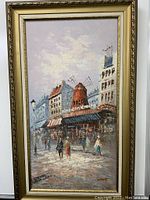 Front view of oil painting on canvas in gold frame depicting street scene with windmill building and pedestrians.