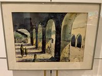 Framed watercolor painting showing architectural arches and shadows with two figures and a signature on the lower right, including visible tear on upper right side under glass.