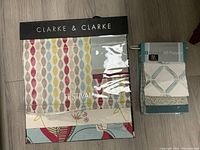 Photo showing Clarke & Clarke fabric sample book with colorful patterns next to a smaller Duralee fabric sample book with blue and white geometric fabric swatches.