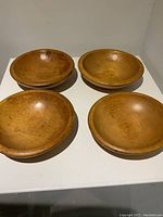 Four vintage teak Mid-Century Modern bowls arranged in a group on white surface showing wood grain and shape.