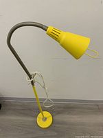 Full view of tall vintage yellow floor lamp with bendable neck and circular yellow base.