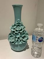 Front view of turquoise ceramic vase with hand-made flower petals and a water bottle for scale.