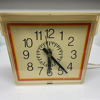 Front view of the vintage 1970s square electric clock showing the dial and hands.