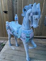 Front view of the wooden horse with a water bottle on its back for size reference, showing pastel colored carved details.