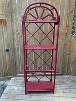 Front view of red bamboo etagere showing two shelves and lattice side panels in a chinoiserie style with arched top and decorative twine accents.