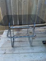 Side table showing smoked glass top with rounded corners and chrome tubular base with rust spots.