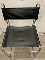 Front view of vintage MCM chair showing black vinyl seat and backrest framed by chrome tubular cantilever frame.