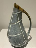 Side view of jug vase showing textured blue-gray glaze with cream raised lines and gold rim and handle.
