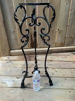 Front view of black vintage metal plant stand with bottle placed at base for scale