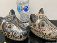 Pair of Mexican Tonala hand painted clay wolf sculptures with abstract polychrome designs shown on a black surface next to a water bottle for scale.