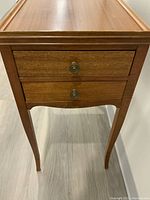 Front view of the vintage satinwood side table showing two drawers with round metal knobs and tapered legs.