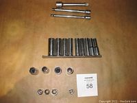 Photo showing an assortment of chrome-finished deep sockets arranged on a brown surface, including some smaller sockets and a few socket adapters or reducers, plus a 1/2 inch drive extension at the top.