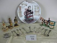 Group photo showing all items including plate, 12 silver spoons, and 4 figurines on a fabric surface.
