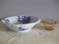 Blue floral ceramic wash basin and pink depression glass floral frog shown side by side