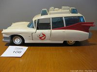 Side view of the white Ghostbusters Ecto-1 toy car on table showing red tail fin, Ghostbusters logo, and blue lights on roof.