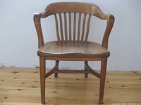 Front view of vintage Krug solid oak banker's chair showing curved armrests, vertical back slats, contoured seat, and sturdy square legs.