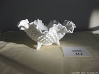 Side view of the white milk glass scalloped bowl standing on three feet, showing hobnail texture and ruffled edge.