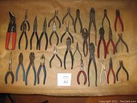 Wide view of 29 hand tools including pliers, cutters, crimpers on a tan background.