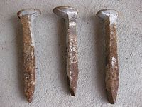 Close-up view of three used railroad spikes showing rust and signs of wear on a gray surface.
