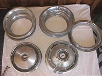 Chrome Chevrolet rally rim trim rings and hubcaps laid on white cloth, showing condition and components in the lot.