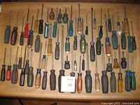 Top-down view of 60 assorted screwdrivers laid out on a flat surface showing varied handle colors and shaft sizes.
