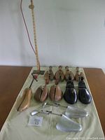 Photo showing 9 wooden shoe stretchers with adjustable metal rods, 2 clear plastic shoe stretchers, vintage dressmaker's chalk hem marker, and a wooden tape measure in background.