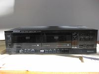 Front view of Kenwood stereo double cassette deck showing entire unit with cassette slots, buttons, and labels visible.