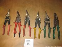 Photo showing six tin snips arranged side by side on a brown surface with a MaxSold lot card labeled 45.