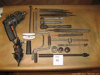 Photo showing a Black & Decker corded drill, Craftsman rotary tool, metal files, ratchets, torque wrench, and sockets laid out on a wooden surface.