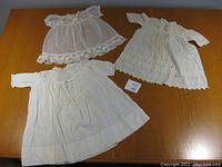 Three vintage baby dresses laid out on a wooden table showing different styles and lace details.
