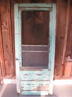 Front view of vintage wooden screen door showing turquoise paint with chipping and wood panels.