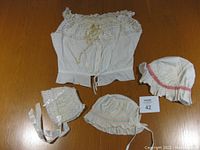 Set of a vintage cotton lace and ribbon top laid flat with three cotton baby bonnets arranged around it, all items on wooden surface.