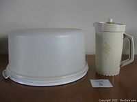 Front view of the vintage Tupperware cake carrier with its opaque dome lid alongside the beige Tupperware juicer with a handle and lid.